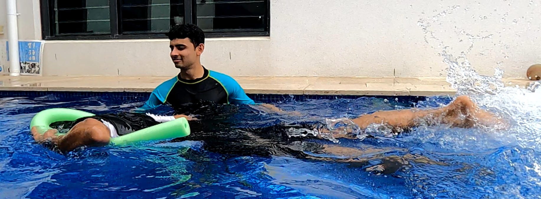 Karan supervising an adult swimmer practising kicking with a pool noodle