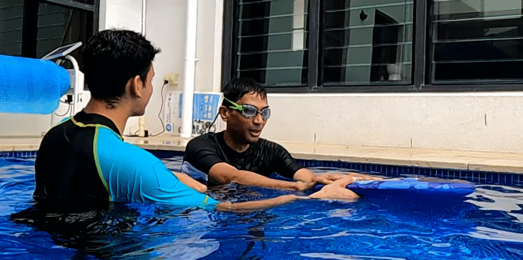 Karan coaching an adult student with a kickboard in a backyard pool